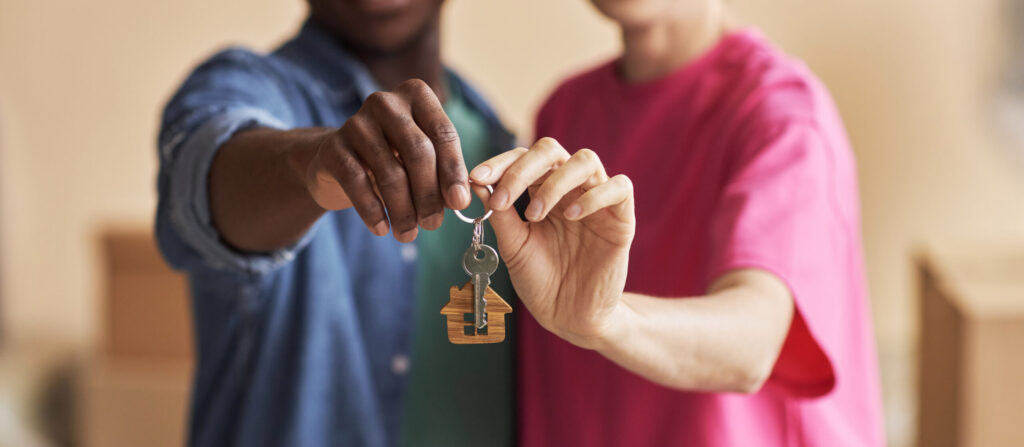 Two people holding a key with a house keychain attached to it.