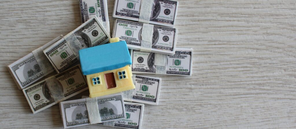 A small clay house overtop a pile of money.