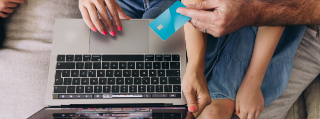 A group of people sitting on the couch together. The person sitting in the center is holding a laptop while another person is handing them a credit card.