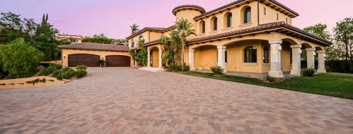 An exterior shot of a luxury home in Hidden Hills, California. It has an expansive driveway that leads to a two-door garage.