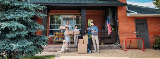 family with cardboard boxes and labrador dog standing on country house porch, moving home concept