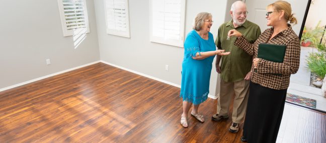 Female Real Estate Agent Handing New House keys to senior adult couple in new home.