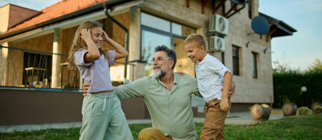 Grandfather is playing with his grandchildren in the backyard of a house, creating happy memories that will last a lifetime