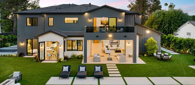 Luxurious modern home with pool. It has several lawn chairs, outdoor seating, and plenty of windows to bring in light. It is sunset in the photo.
