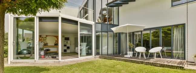 Neat paved patio with sitting area in front of a modern home with large glass windows.