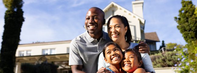 A happy family with children standing in front of a new home.