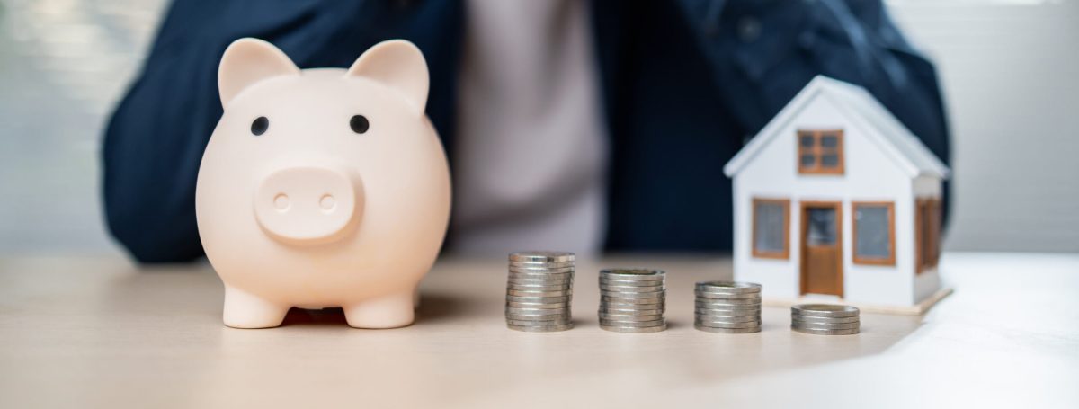 A person sits with piggy bank and coins, contemplating finances