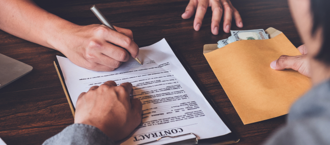 Someone signing a contract while giving an envelope of money to the person sitting across from them.
