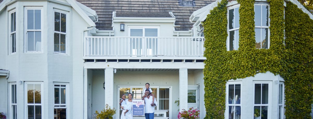 A family standing outside of their newly purchased home. It is a gran home with ivy covering one side of the home.